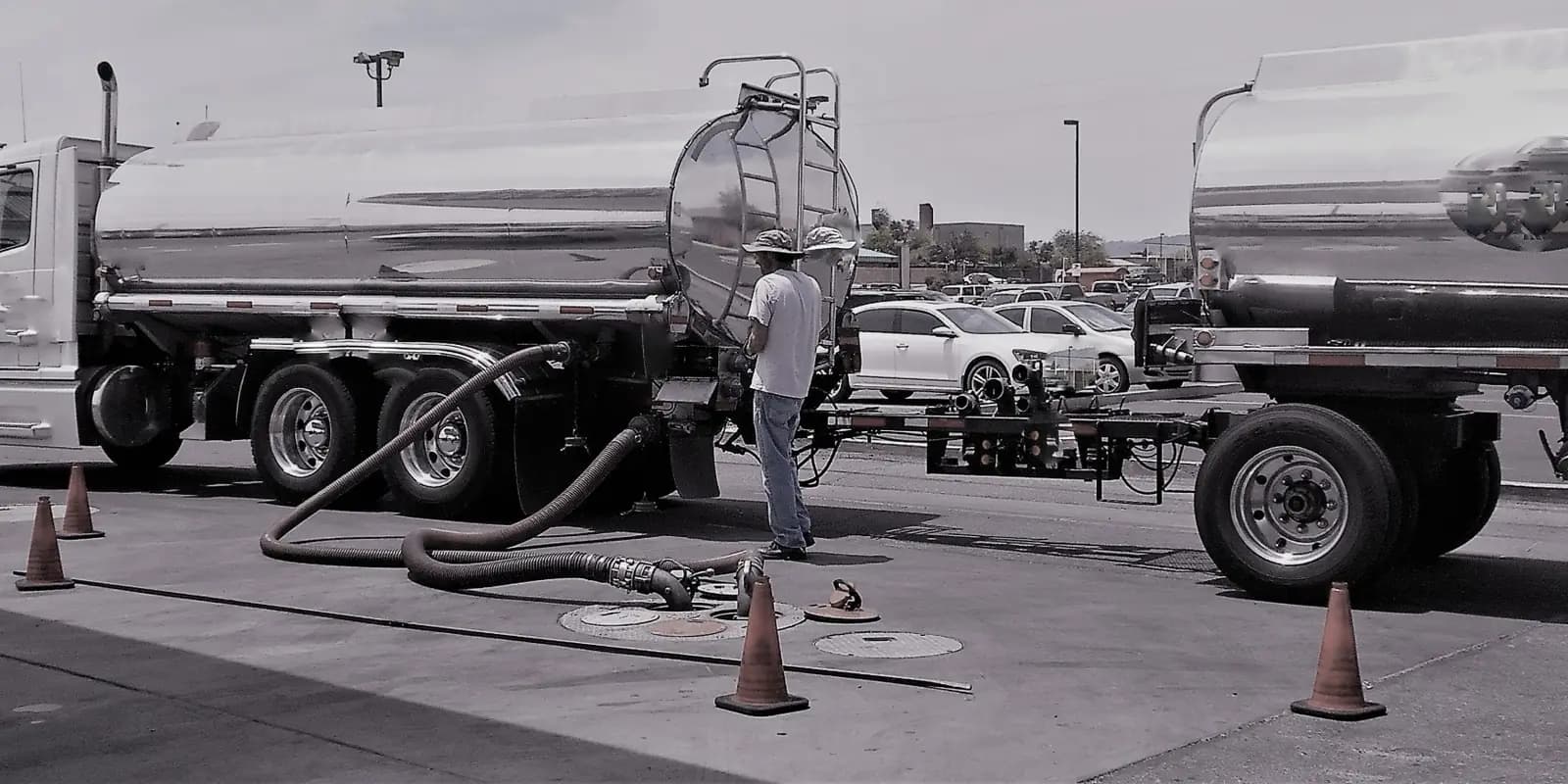 Operator connecting hoses between a tanker truck and an underground tank, with safety cones set out